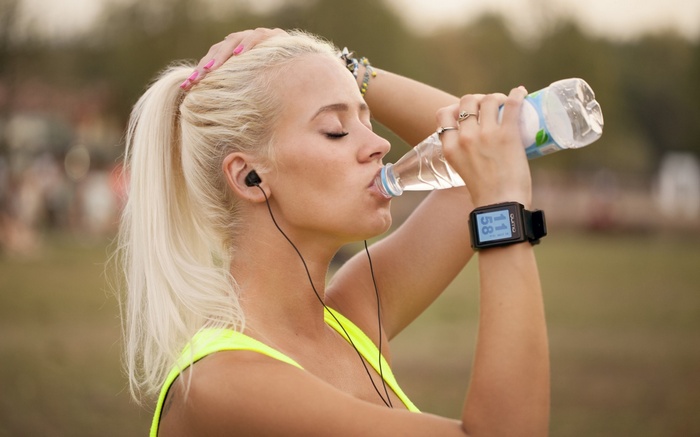 Woman drinking water from bottle with headphones and smartwatch