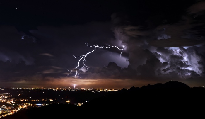Lightning strikes over a city at night with mountains