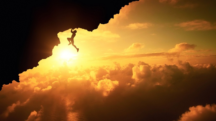 Silhouette of a man rock climbing at sunset over clouds