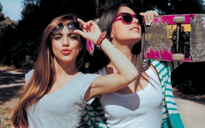 Two women with sunglasses and a skateboard outdoors