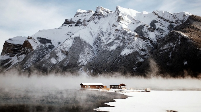 Snowy mountains over a misty lake with cabins