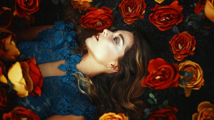 Woman in blue dress lying among red and yellow roses