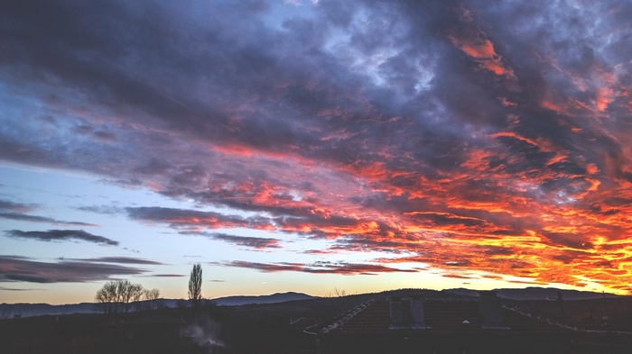 Sunset clouds over a dark landscape with mountains