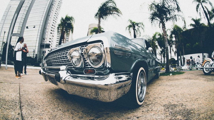 Lowrider car parked near palm trees and modern buildings
