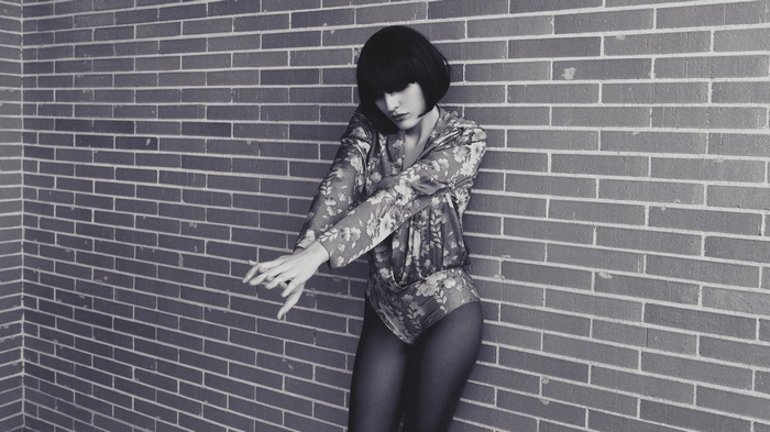 Woman in floral leotard leaning against brick wall