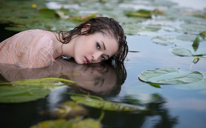 Woman in pink dress submerged in water with lily pads