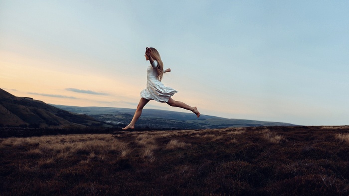 Woman in white dress jumping in a landscape