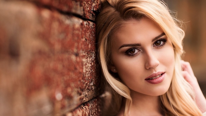 Woman with blonde hair leaning against a brick wall