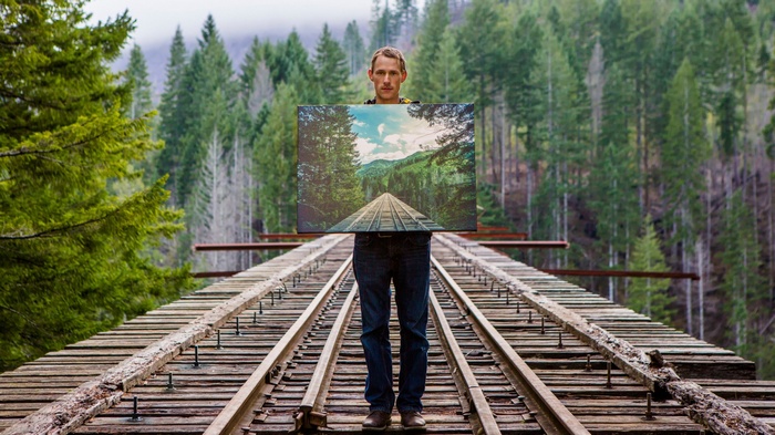 Man holding a painting on a railway bridge