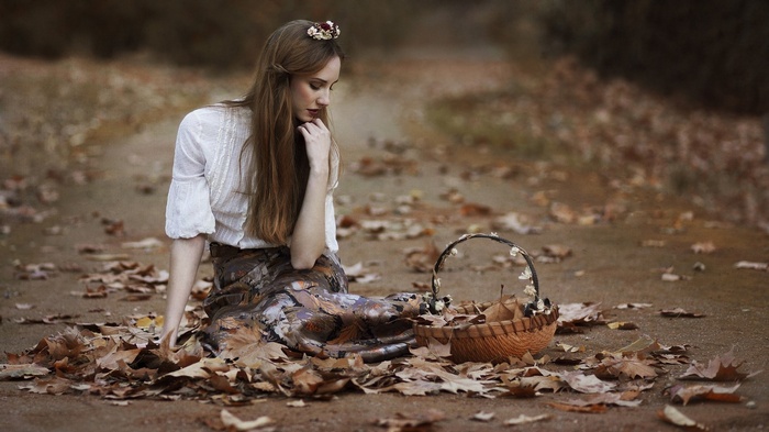 Woman sitting on the ground with fallen leaves and a basket