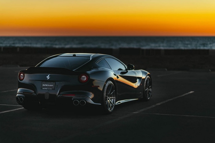 Black Ferrari F12berlinetta parked by the ocean at sunset