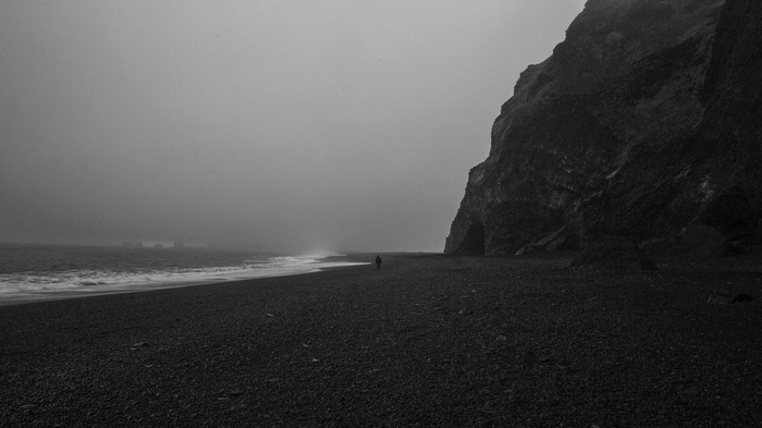 Person walking on a black sand beach with a cliff