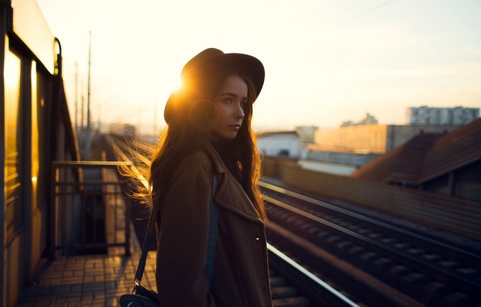 Woman in hat and coat at sunset near railway