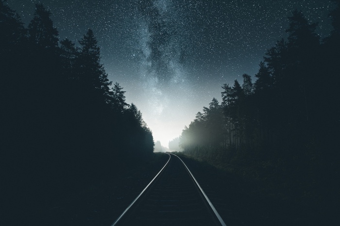 Railway through a forest under the starry night sky
