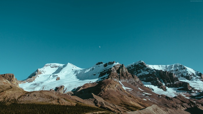 Snow-capped mountains under a clear blue sky with a crescent moon