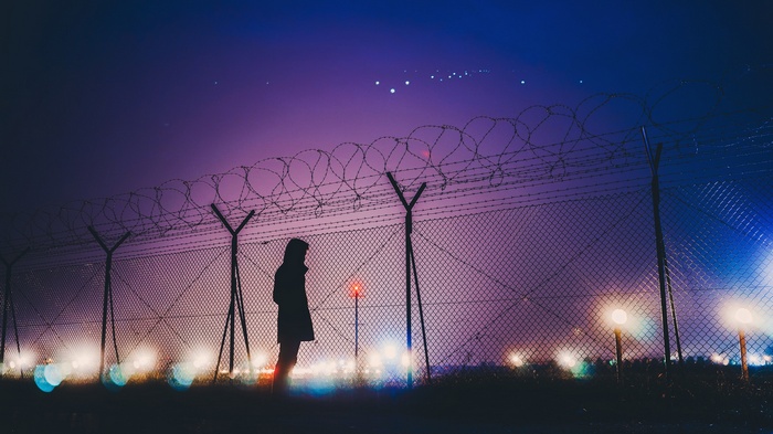 Person standing by a barbed wire fence at night