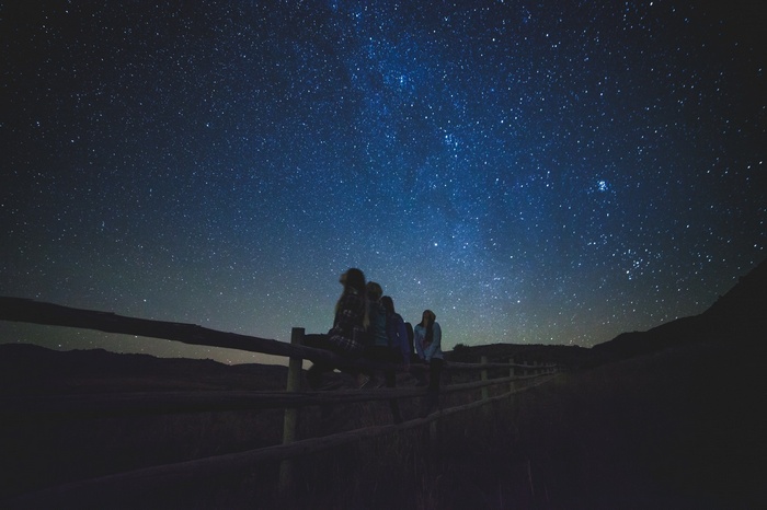 People sitting on a fence under a starry night sky