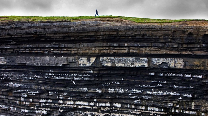 Person walking on cliff edge in Ireland with birds
