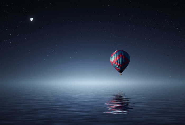 Hot air balloon floating over water at night under stars