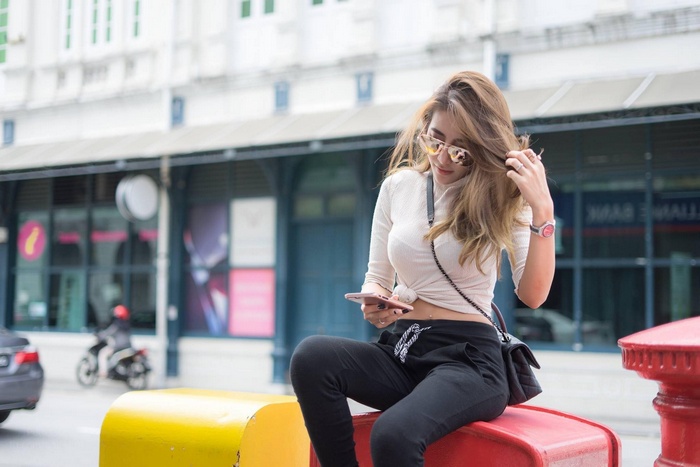 Phasinee Boonrod sitting on a red post with a phone
