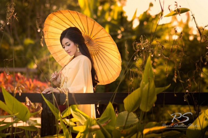 Asian woman holding a yellow umbrella in a garden