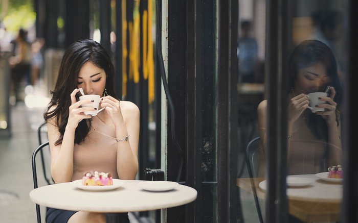 Asian woman drinking coffee at a cafe with cake
