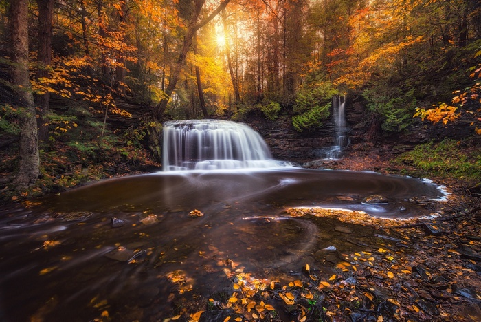 Waterfall in a colorful forest during fall with sunlight