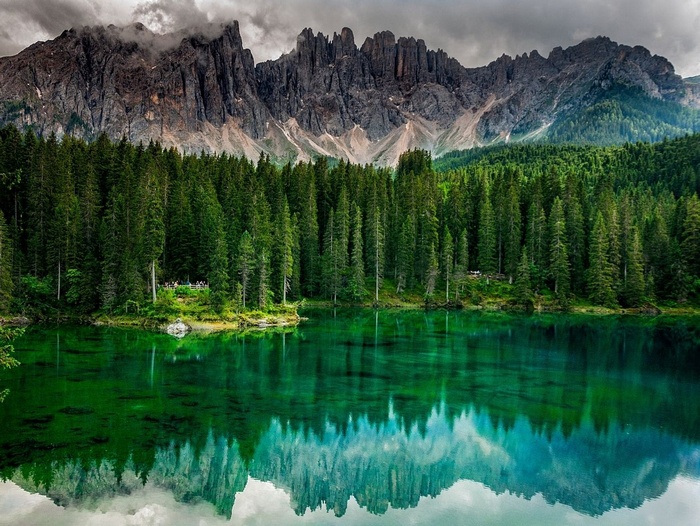 Emerald lake reflecting pine forest and jagged mountains