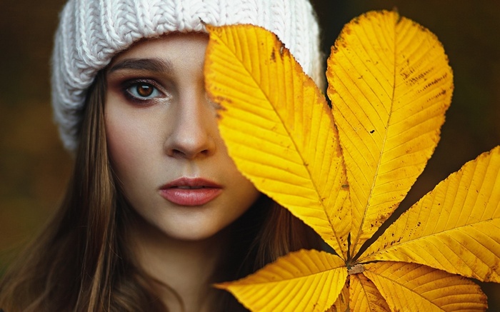 Woman wearing a white beanie holding yellow leaves