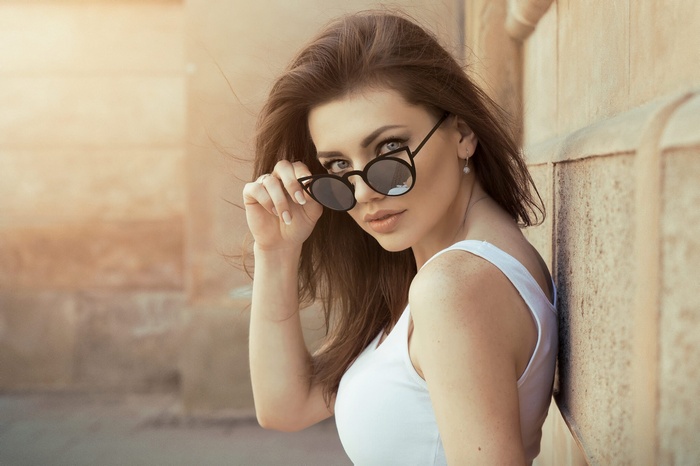 Woman wearing sunglasses and tank top leaning against a wall