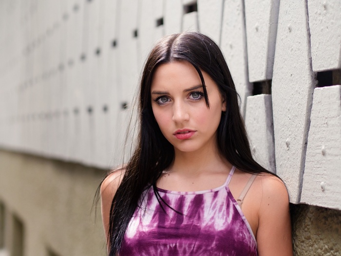 Woman in a purple tie-dye top leaning against a wall