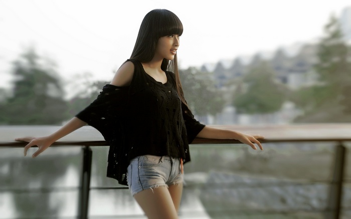 Woman with bangs wearing black top and jean shorts