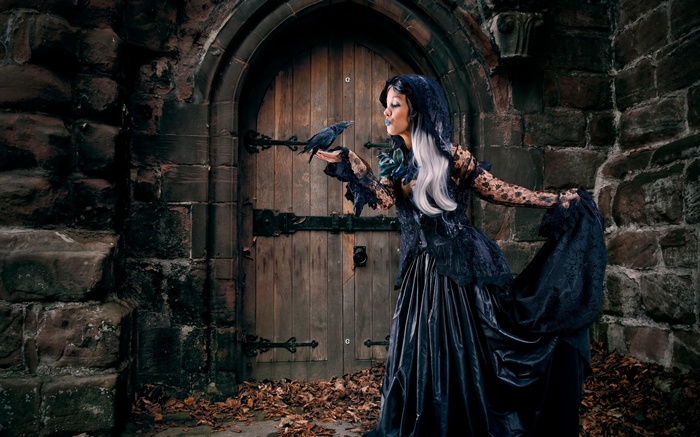 Woman in black dress with crow in front of wooden door