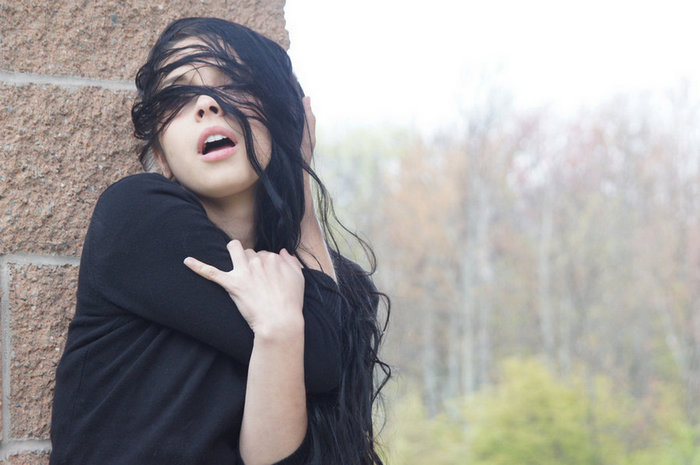 Woman with hair covering face leaning against wall