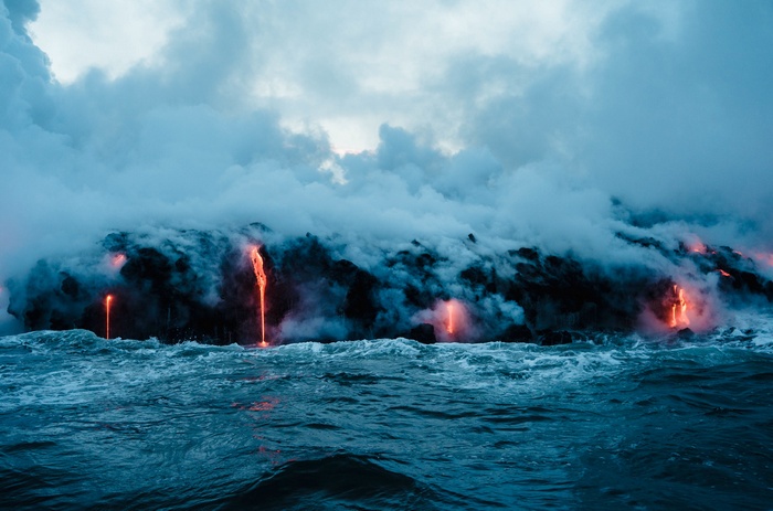 Lava flowing into the ocean with steam and clouds