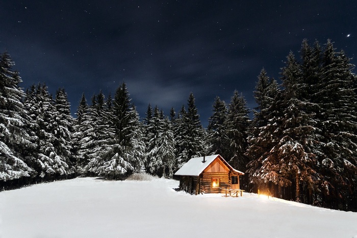 Log cabin in snowy forest under starry night sky