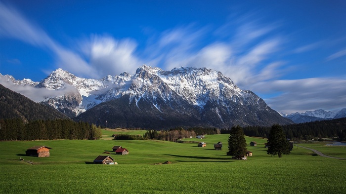 Snowy mountain landscape with green fields and cabins