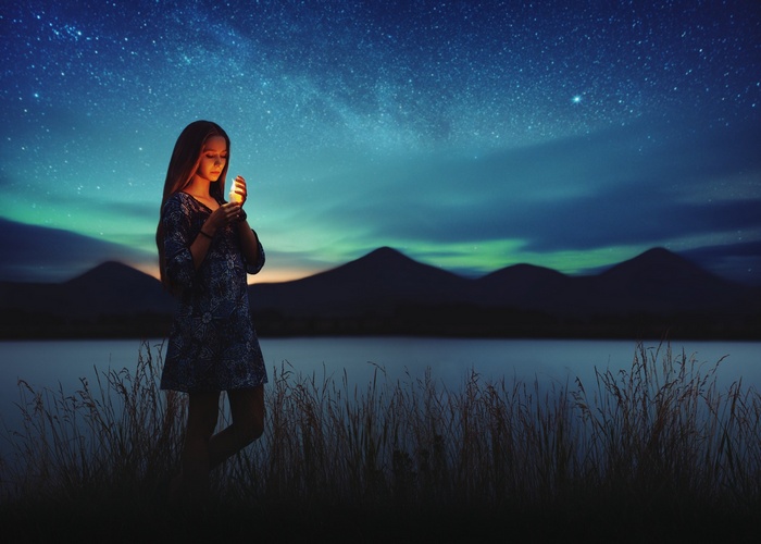 Girl holding a candle by a lake under the stars