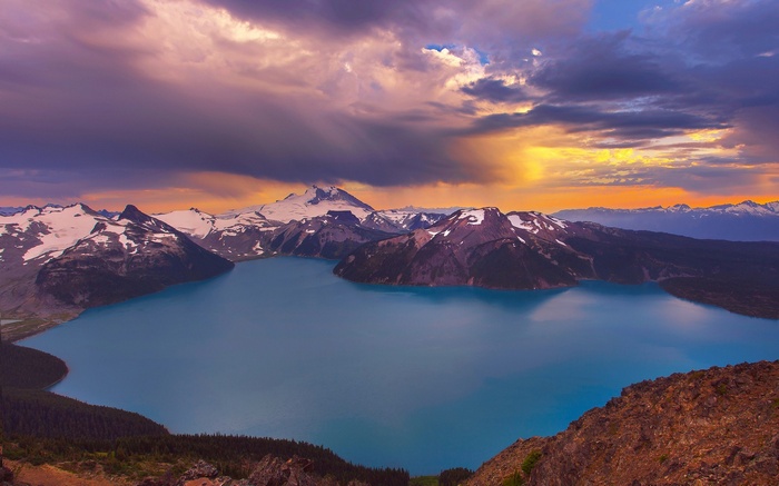 Turquoise lake surrounded by snow-capped mountains at sunset