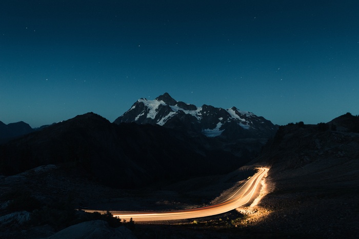 Mountain road with light trails under starry night sky