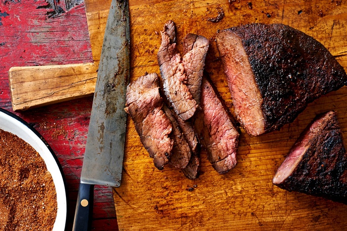 Sliced smoked meat on a cutting board with a knife