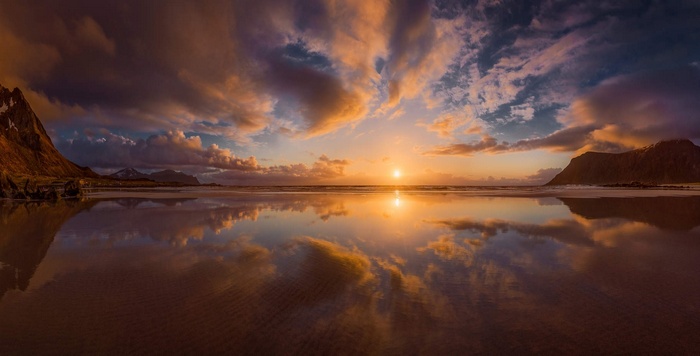 Sunset over a calm beach with mountains and reflection