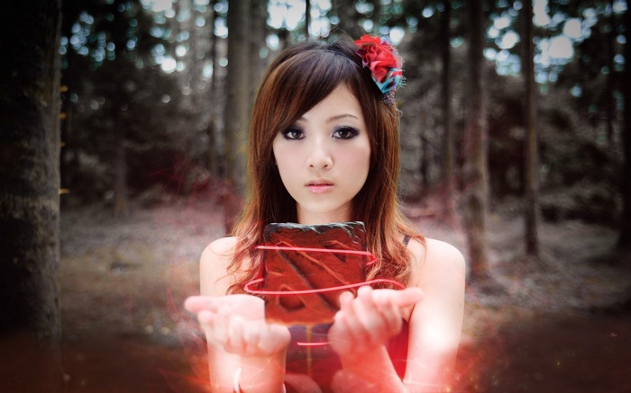 Asian woman holding a glowing red object in a forest
