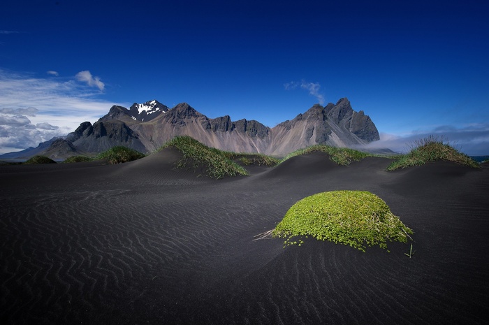 Black sand dunes and mountains under a blue sky