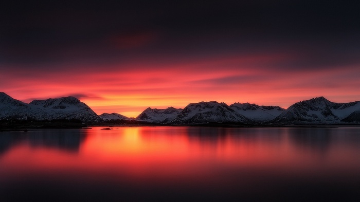 Snowy mountains reflected in a lake at sunset