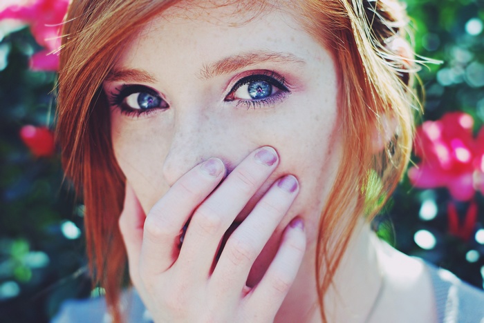 Woman with red hair and blue eyes covering mouth