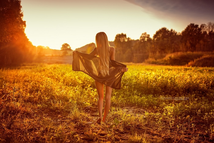 Woman with long blonde hair in a field at sunset