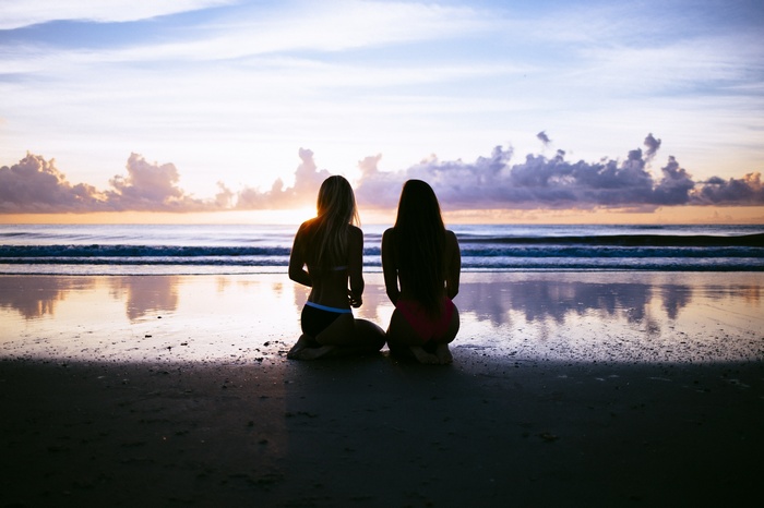 Two women kneeling on a beach at sunset