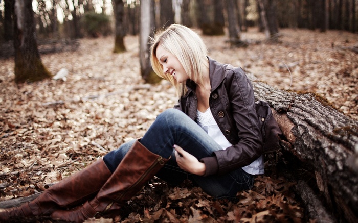 Woman in jacket and boots sitting on leaves