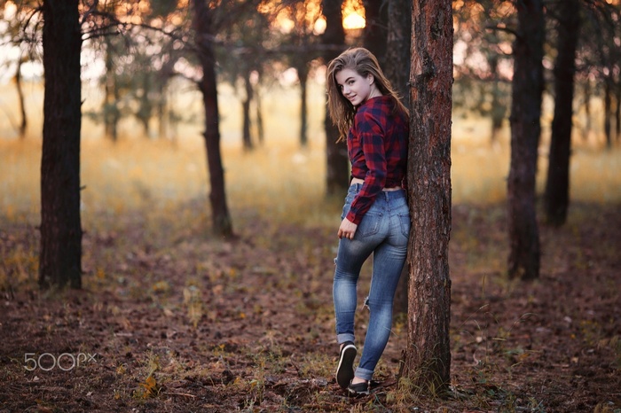 Woman in plaid shirt and ripped jeans leaning against a tree
